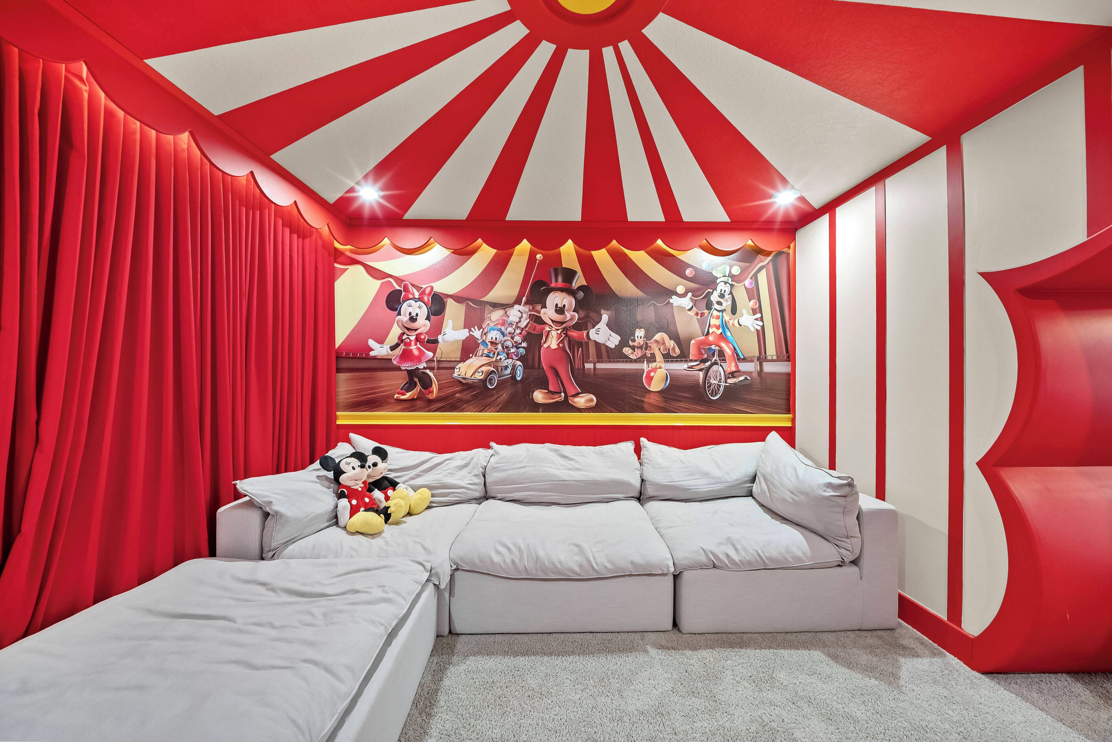 Una habitación con un gran mural de personajes de caricatura, un techo a rayas rojas y blancas, y una cama con un peluche de Mickey Mouse.