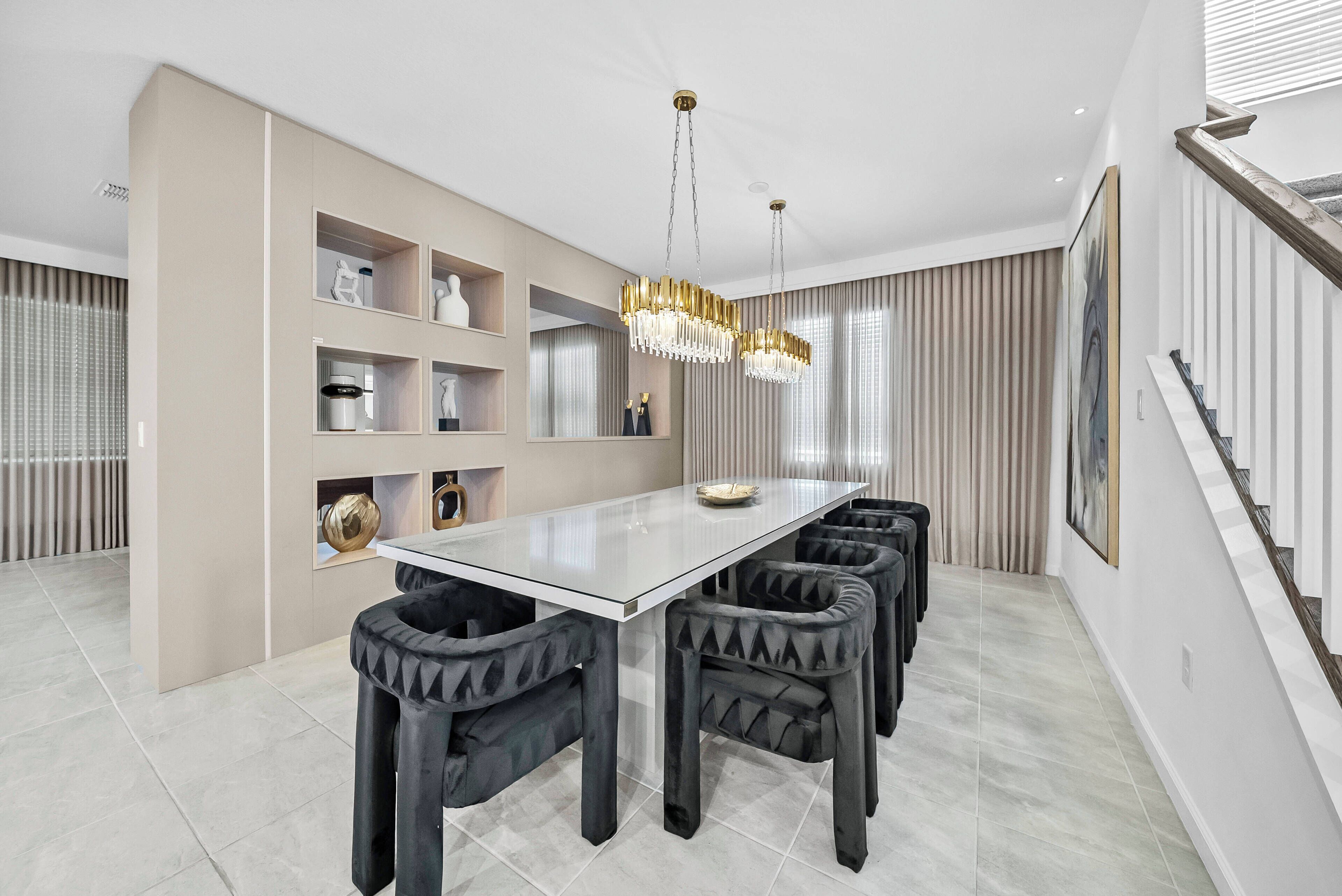A modern dining area with a glass-top table, black upholstered chairs, and a chandelier.