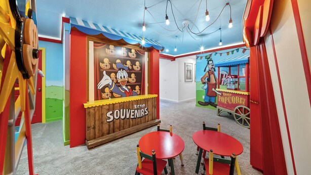 A room with a wooden wall display labeled 'Big Top Souvenirs,' a popcorn cart, and two red tables with chairs. - 9BR house sleeps 18 with spa and private pool\Racing Simulator (Kissimmee)