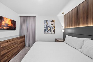 Una habitación de hotel moderna con una cama grande, un aparador de madera, un cuadro y un televisor instalado en la pared.