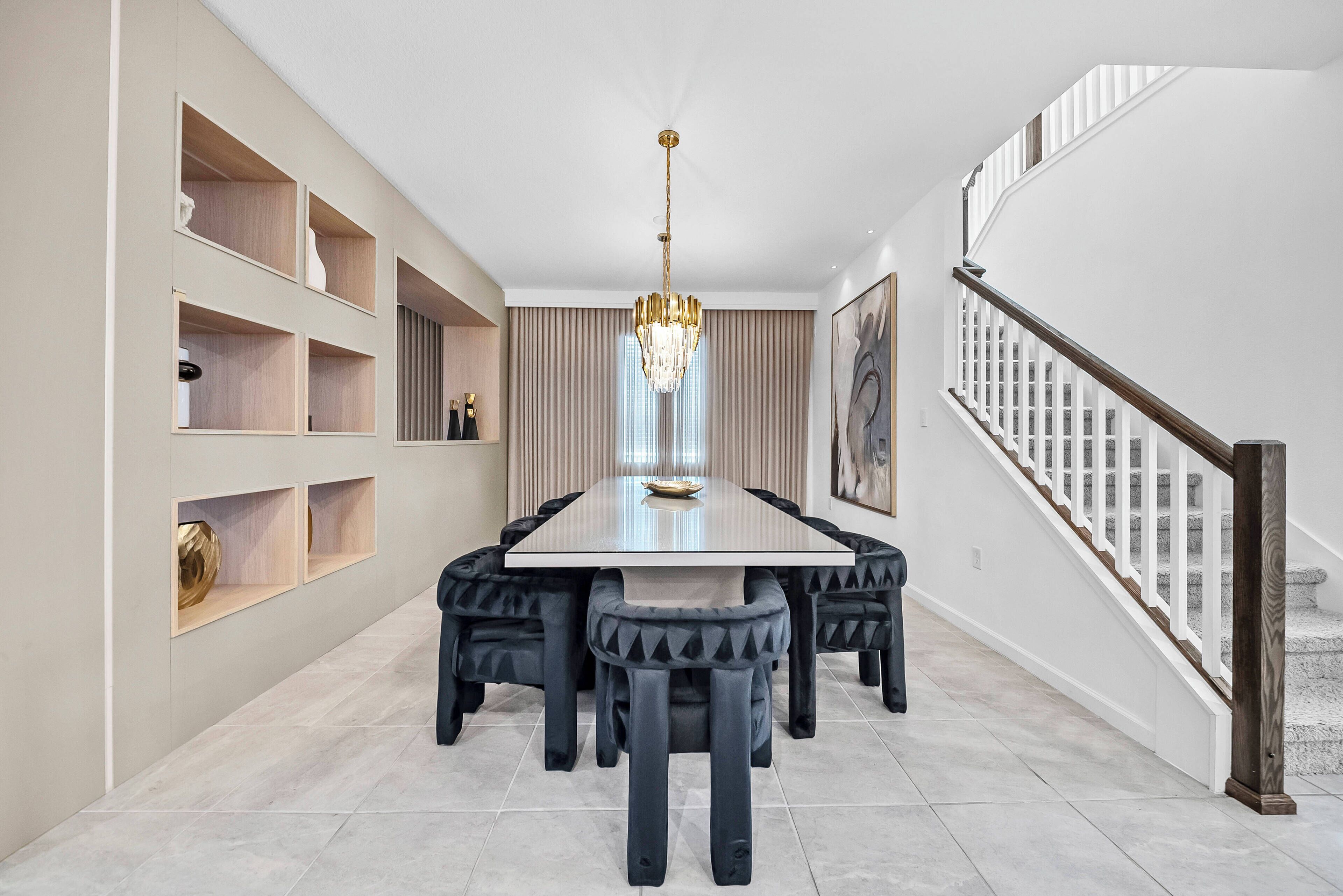 Un comedor con mesa rectangular, sillas tapizadas en negro, una araña y estanterías empotradas con objetos decorativos.