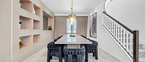 Un comedor con mesa rectangular, sillas tapizadas en negro, una araña y estanterías empotradas con objetos decorativos.