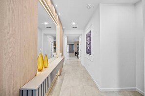 A modern hallway with a wooden accent wall, a reception desk with decorative vases, and a framed artwork on the wall. - 9BR house with private pool at Solara Resort\Racing Simulator (Kissimmee)