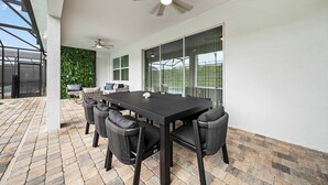 An outdoor patio with a black table and chairs, a ceiling fan, and a view of a green wall and a glass door. - 9BR house sleeps 18 with spa and private pool\Racing Simulator (Kissimmee)