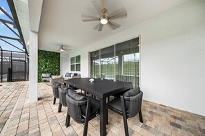 Eine Terrasse im Freien mit einem schwarzen Tisch und Stühlen, einem Deckenventilator und Blick auf eine grüne Wand und eine Glastür.