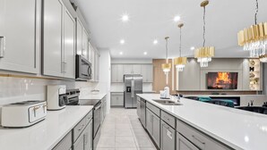 A modern kitchen with stainless steel appliances, white cabinetry, and pendant lighting. - 9BR house sleeps 18 with spa and private pool\Racing Simulator (Kissimmee)