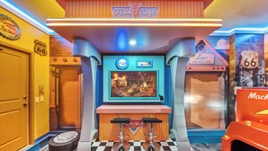 A children's play area with a checkered floor, a TV screen, and a counter with a logo. - 9BR house sleeps 18 with spa and private pool\Racing Simulator (Kissimmee)