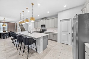 Cocina moderna con una isla central, taburetes de bar, refrigerador de acero inoxidable y una escalera que lleva a otro nivel.