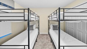 Ein Zimmer mit Etagenbetten, Teppichboden, einer weißen Tür und einem Fenster mit Jalousien.