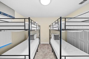 Ein Zimmer mit Etagenbetten, Teppichboden, einer weißen Tür und einem Fenster mit Jalousien.