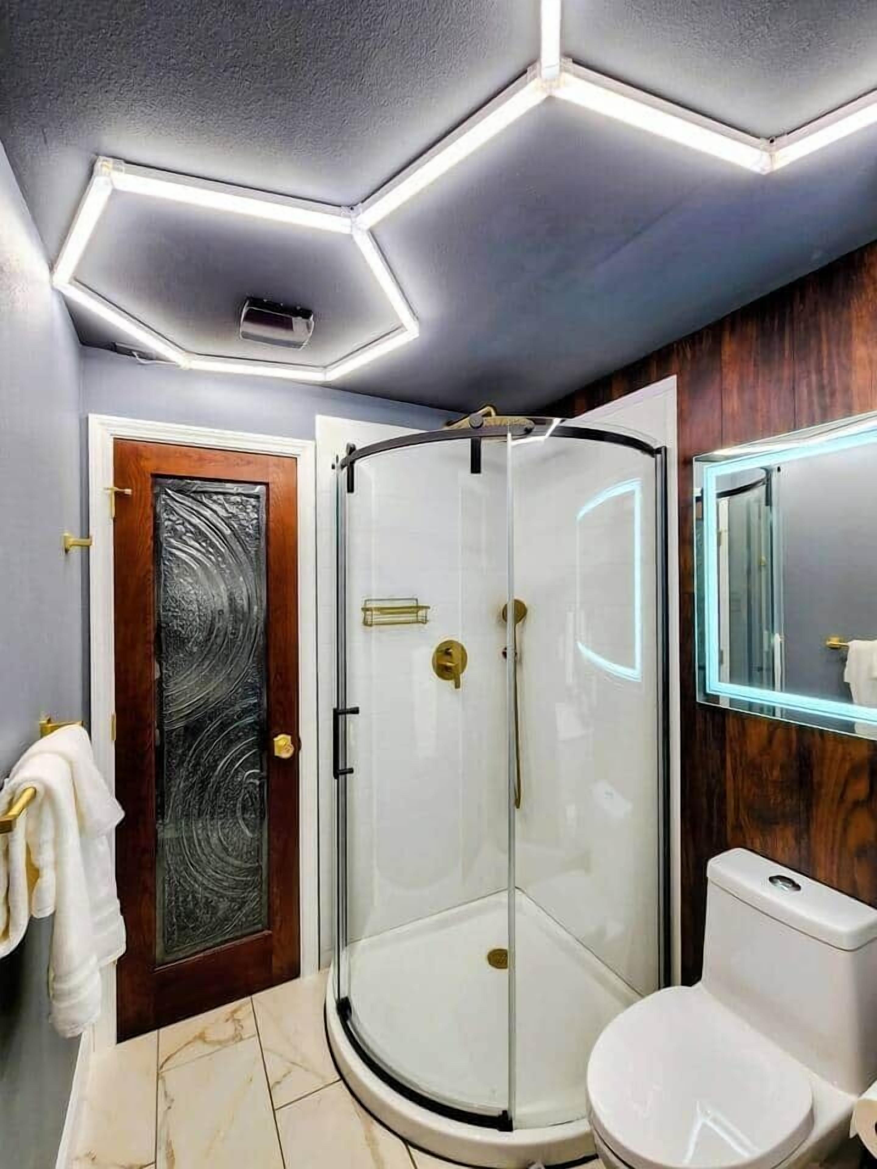 Casa de banho moderna com cabine de duche em vidro, sanita branca e porta de madeira com painel de vidro texturizado.