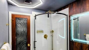 Casa de banho moderna com cabine de duche em vidro, sanita branca e porta de madeira com painel de vidro texturizado.