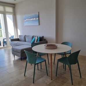 A living room with a grey sofa, teal chairs, a round table, and a painting on the wall. - Buenaventura Luxury Condo Beach Club • Golf (Río Hato)