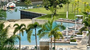 Een resort met een zwembad, ligbedden, palmbomen en uitzicht op de oceaan.