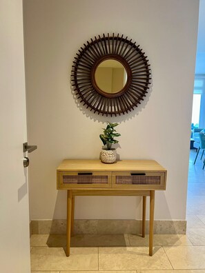 Une console en bois, surmontée d’un miroir décoratif, avec une plante en pot posée sur le plateau et une porte située à gauche.