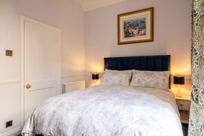 Een slaapkamer met een bed, bedlampjes, een deur en een lijst aan de muur.