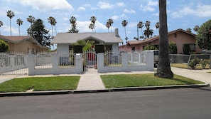 A residential property with a gated entrance, a well-maintained lawn, and a row of palm trees in the background. - Charming 3-bedroom house centrally located in Los Angeles with AC (Los Angeles)