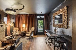 A room with a stone wall, a chandelier, a large mirror, a dining table with bar stools, and a view through a door. - Music Row | 5 Legend-Themed Suites | Sleeps 26 (Nashville)