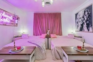 A pink-themed bedroom with two beds, a neon sign, and a large portrait on the wall. - Music Row | 5 Legend-Themed Suites | Sleeps 26 (Nashville)