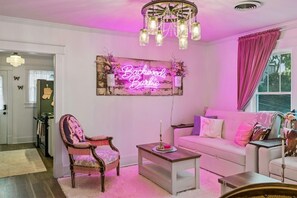 Ein Wohnzimmer mit einer Neonreklame, einem Chandelier, einem Sofa und einem Sessel.