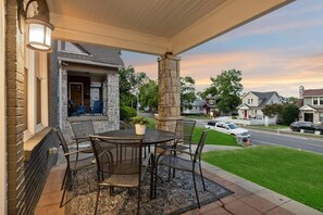 A covered patio with a table and chairs, a stone pillar, and a view of a residential street. - Music Row | 5 Legend-Themed Suites | Sleeps 26 (Nashville)