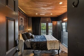 A bedroom with a bed, a bench, a fireplace, and a view of the outdoors. - Music Row | 5 Legend-Themed Suites | Sleeps 26 (Nashville)