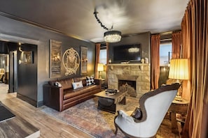 A modern living room with a fireplace, leather sofa, armchair, and a chandelier. - Music Row | 5 Legend-Themed Suites | Sleeps 26 (Nashville)