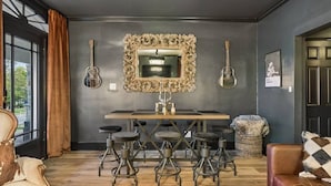 A room with a dark wall, a large ornate mirror, a wooden table with bar stools, and a guitar on the wall. - Music Row | 5 Legend-Themed Suites | Sleeps 26 (Nashville)