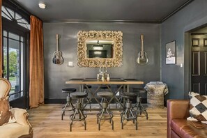 A room with a dark wall, a large ornate mirror, a wooden table with bar stools, and a guitar on the wall. - Music Row | 5 Legend-Themed Suites | Sleeps 26 (Nashville)