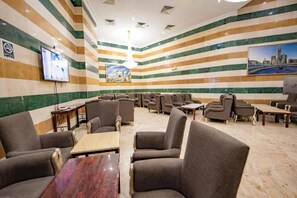 Eine Hotellobby mit gestreifter Wandgestaltung, mehreren Sitzbereichen, einem Fernseher und einem Stadtbildgemälde.