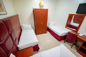 Ein Hotelzimmer mit zwei Einzelbetten, einem Holzschrank, einem Schreibtisch mit Stuhl und einem an der Wand befestigten Fernseher.