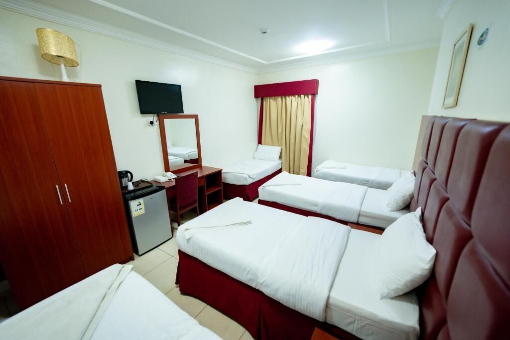 A hotel room with four beds, a desk, a television, a wardrobe, and a small kitchenette.