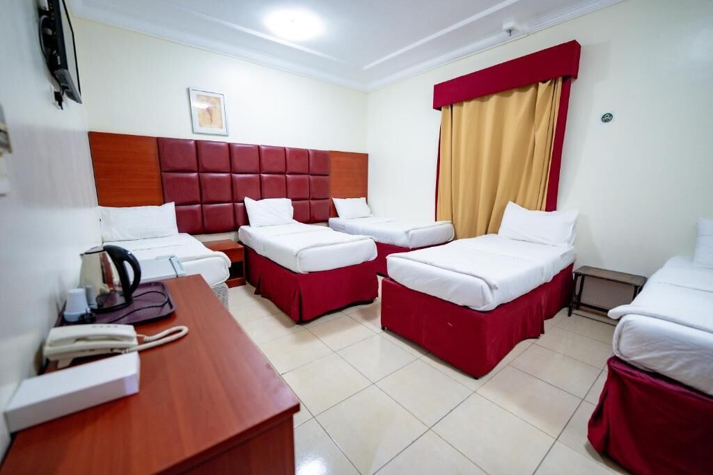 Habitación de hotel con escritorio de madera, dos camas individuales, una cama doble y cabecera roja.