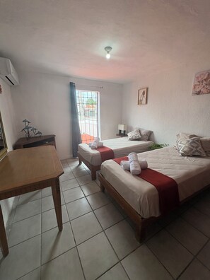 A hotel room with two beds, a desk, a window with curtains, and a ceiling light. - Casa Céntrica, Cerca de la Playa. Acogedora con alberca en la residencial. (Cancún, QROO)
