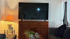En stue med et fladskærms-TV, en sofa, et sofabord med dekorative genstande og en lampe.