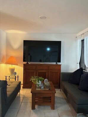 Ein Wohnzimmer mit Flachbildfernseher, einer Couch, einem Couchtisch mit Dekoration und einer Lampe.