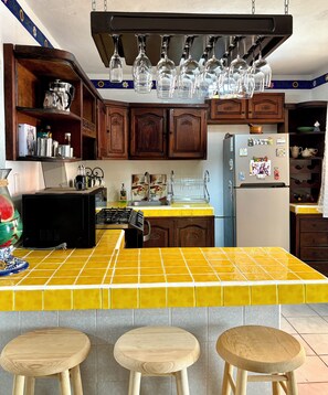 A kitchen with wooden cabinets, a yellow-tiled island, and a stainless steel refrigerator. - Casa Céntrica, Cerca de la Playa. Acogedora con alberca en la residencial. (Cancún, QROO)