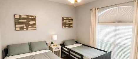 A bedroom with two beds, a ceiling fan, a nightstand, and a window with curtains.