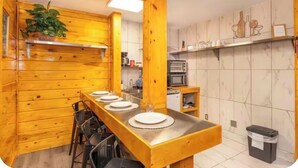 A wooden interior with a long dining table set for four, a kitchen area with appliances, and a trash bin. - Charming Studio 15, Pets Welcome, Near Dollywood, Near The Strip (Pigeon Forge)