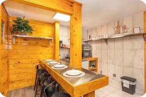 Ein Holzinterieur mit einem langen Esstisch, gedeckt für vier Personen, einer Küchenzeile mit Geräten und einem Mülleimer.