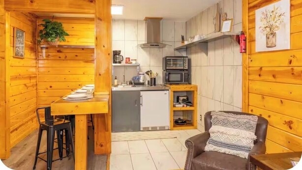 A compact kitchen with a refrigerator, microwave, and toaster oven. There is a dining table with chairs and a small seating area with a cushioned chair. - Charming Studio 15, Pets Welcome, Near Dollywood, Near The Strip (Pigeon Forge)