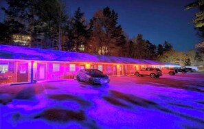 Ein Motel mit mehreren Zimmern, einem Parkplatz und bewaldeter Landschaft im Hintergrund.