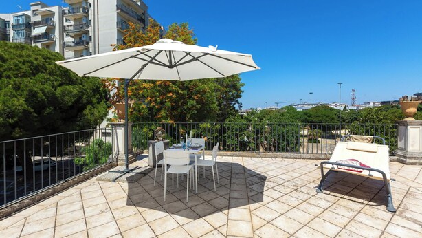 Eine Terrasse im Freien mit Tisch, Stühlen, einem weißen Sonnenschirm und einer Liege.