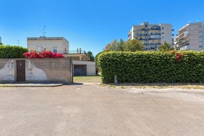 A residential area with a paved entrance, a hedge with red flowers, and multi-story buildings in the background. - Ca` Mele by BarbarHouse (Lecce)
