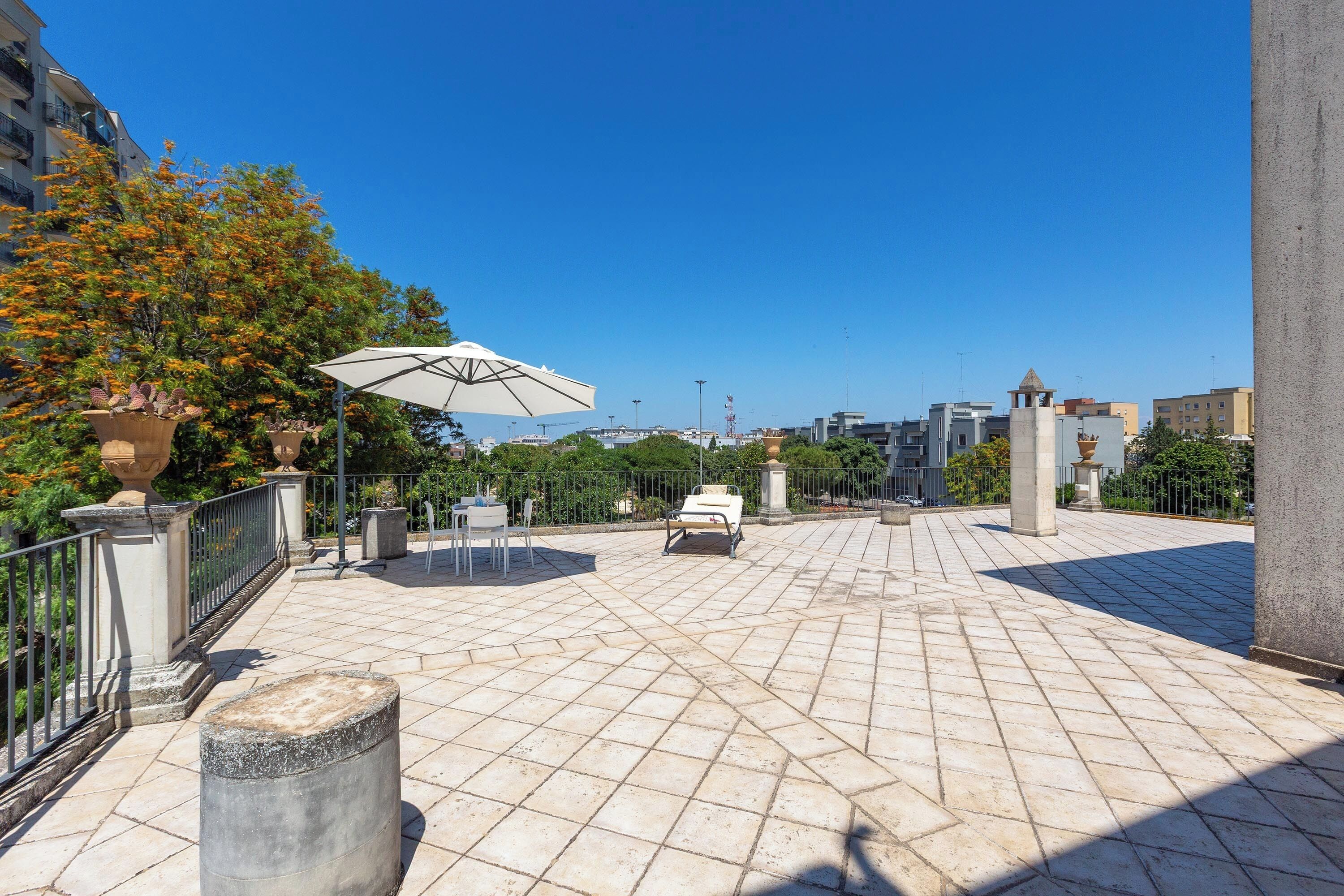 An outdoor patio area with a tiled floor, a white umbrella, and a seating area with a table and chairs.