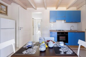 A modern kitchen with blue cabinets, a dining table set with blue and white ceramicware, and a view into the adjacent room. - Ca` Mele by BarbarHouse (Lecce)