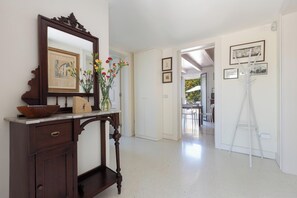 Ein Flur mit einem Holztischchen, einem Spiegel und einer Vase mit Blumen. An der Wand hängen gerahmte Bilder und ein Whiteboard-Ständer.