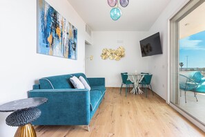 A modern living room with a teal sofa, a small round table, a flat-screen TV, and a glass door leading to an outdoor area. - Casa Sibiana by BarbarHouse (Gallipoli)