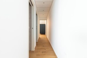 Ein schmaler Flur mit Holzboden und weißen Wänden, der zu einem dunklen Schrank führt.