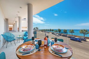 A dining table set with plates, glasses, and a bottle, overlooking a coastal street with parked cars and palm trees. - Casa Sibiana by BarbarHouse (Gallipoli)